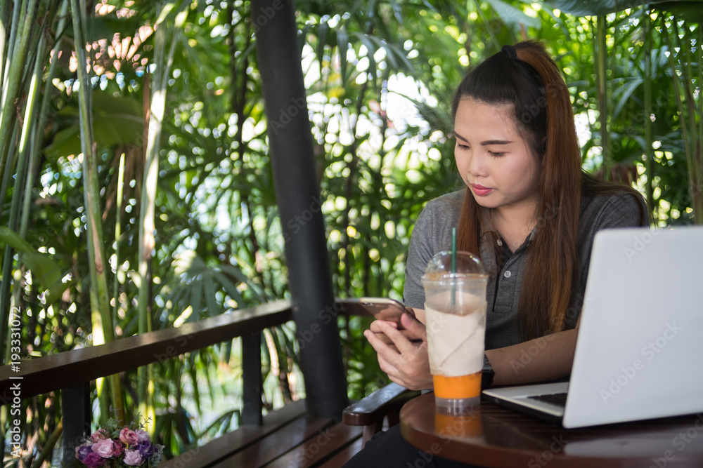 Young woman hold smartphone in coffee cafe, white laptop and iced milk tea on wooden table of brown, business online Young woman hold smartphone in coffee cafe, white laptop and iced milk tea on wooden table of brown, business online