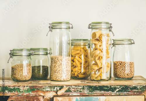 Various uncooked cereals, grains, beans and pasta for healthy cooking in glass jars on rustic table, white background. Clean eating, vegetarian, vegan, balanced dieting food concept