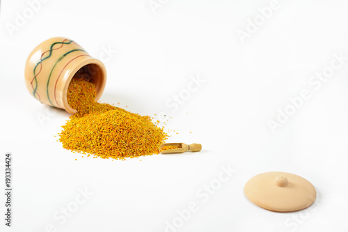 Bee pollen poured out from a small glazed clay pot. Next to the pile of pollen lies one little wooden scoop. In the foreground lies a lid. Selective focus. photo