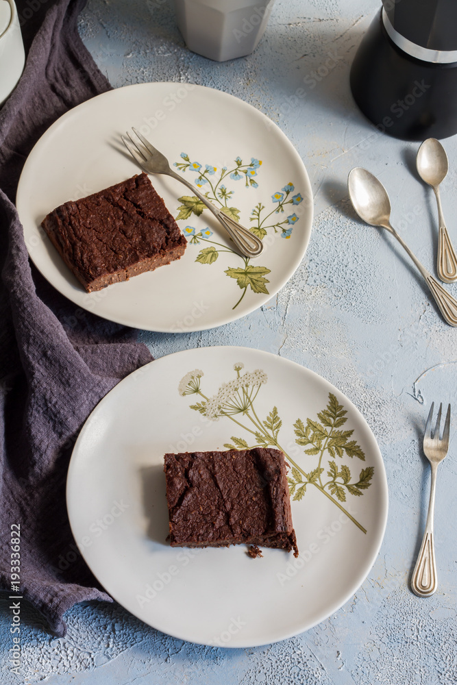 Millet brownie. White plates, cups of coffee and black esspreso maker. White and light blue background. Woolen tapestry. Millet brownie. White plates, cups of coffee and black esspreso maker. White and light blue background. Woolen tapestry.