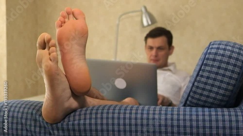 serious business man lying on sofa, working with laptop, waving hands. feet, close-up photo