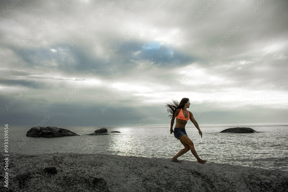 Woman jumping on a rock at sunset on Bakovern Beach, Cape Town. Woman jumping on a rock at sunset on Bakovern Beach, Cape Town.