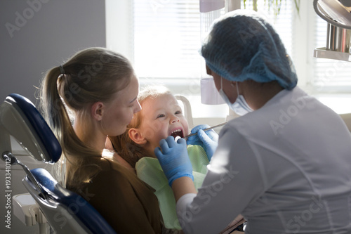 Girl, her mom and the dentist in the dental office, the stomatologist examining the girl using special instruments