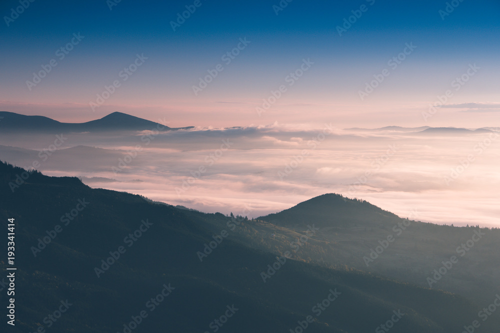 Beautiful landscape in the mountains at sunrise. View of  the foggy hills covered by forest. Retro effect. Traveling concept background.