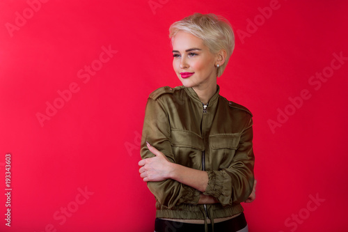beautiful young girl with a smile and with a short hairdo in a jacket on a red background