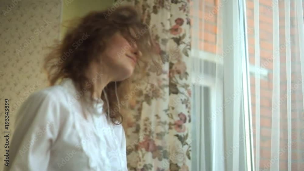 girl curly hair, actively twists her head, playful, listens to music in the headphones by the window, the phone in her hands, dances, singing. portrait girl curly hair, actively twists her head, playful, listens to music in the headphones by the window, the phone in her hands, dances, singing. portrait