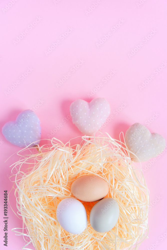 Easter eggs of different colors in a straw nest and decorative textile hearts on a pink background, Top view, Flat lay. Easter concept.