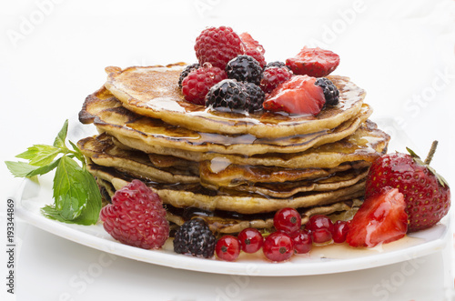 Delicious pancakes with berries and maple syrup on a white background