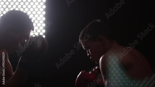 Two athletes in fights without rules during a training battle. Blows, protection, biases. Modeling light in a dark room. Backlighting.