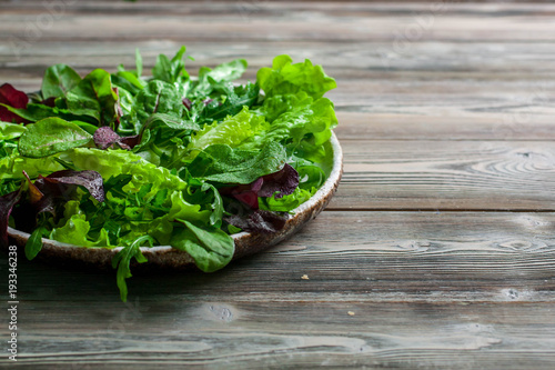 Leaves of fresh lettuce, arugula, spinach and beet sprouts in a plate on a wooden background.