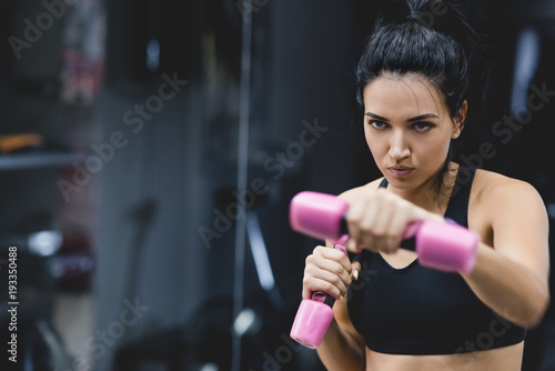Horizontal portrait of strong young woman doing exercise with dumbbells. Fitness European female doing intense training in the gym club. Sport, people, motivation and healthy liefstyle concept.