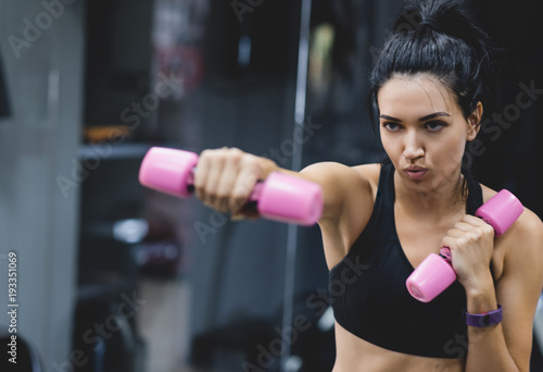 Caucasian strong young woman doing exercise with pink dumbbells. Fitness European female doing intense training in the gym club. Sport, people, motivation and healthy liefstyle concept. Copy space.