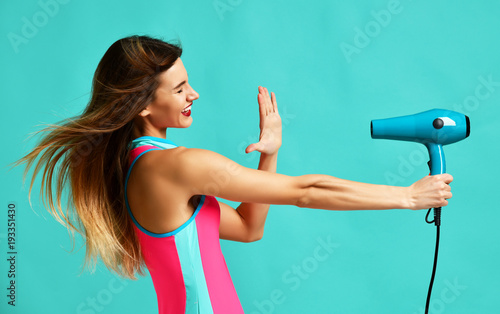 Happy young brunette woman pointing hair dryer on blue mint 