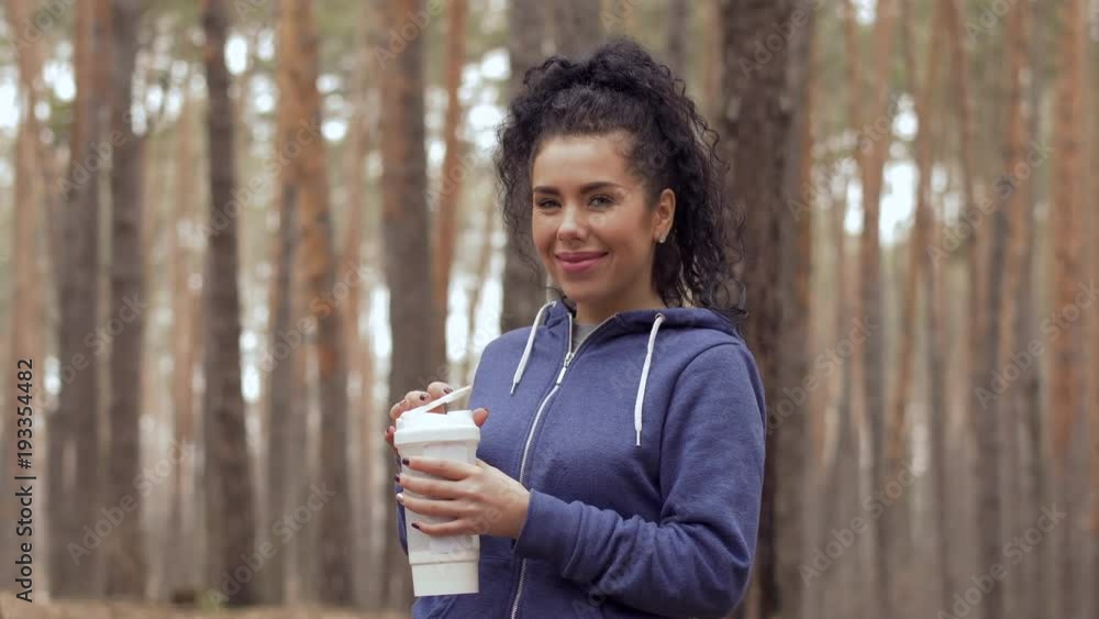 Young beautiful woman drinks water during morning exercises in the forest Young beautiful woman drinks water during morning exercises in the forest