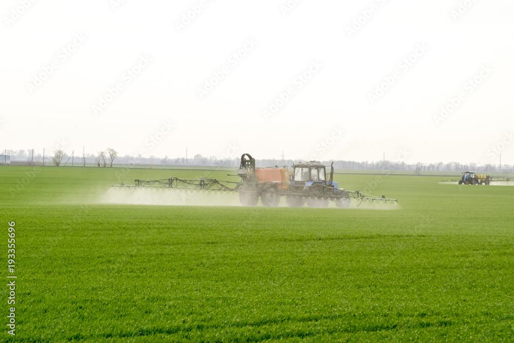 Tractor with high wheels is making fertilizer on young wheat. The use of finely dispersed spray chemicals. Tractor with a spray device for finely dispersed fertilizer. Tractor with high wheels is making fertilizer on young wheat. The use of finely dispersed spray chemicals. Tractor with a spray device for finely dispersed fertilizer.