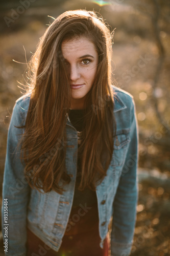 young woman with long brown hair looking into camera with sun at her back