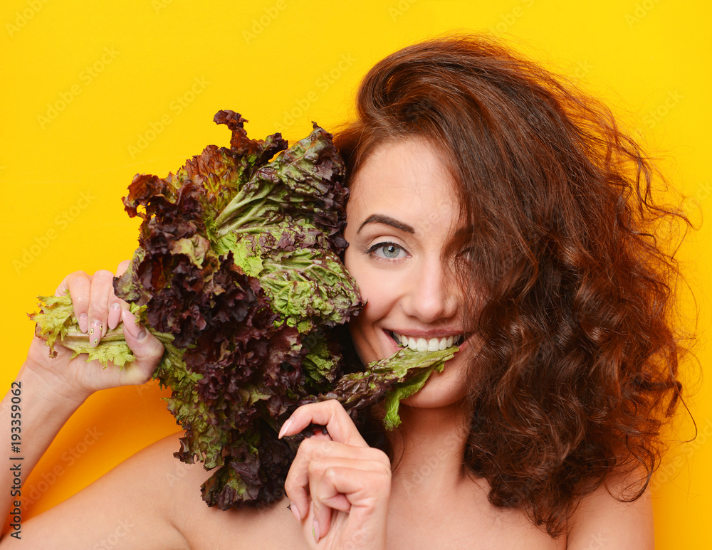 Pretty curly hair woman eat lettuce salad looking at the corner on yellow background Pretty curly hair woman eat lettuce salad looking at the corner on yellow background