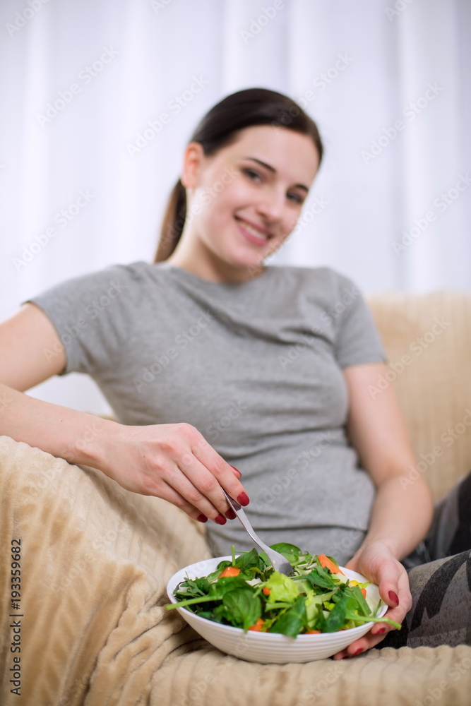 Woman in sportswear with plate of vegetarian vegetable salad. Young sporty model at livingroom. Health, beauty and fitness concept. Woman in sportswear with plate of vegetarian vegetable salad. Young sporty model at livingroom. Health, beauty and fitness concept.