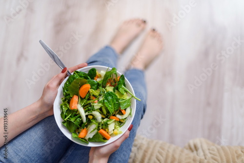 Sitting woman hold and eating vegan salad with arugula, celery and spinach in white plate. Healthy eating