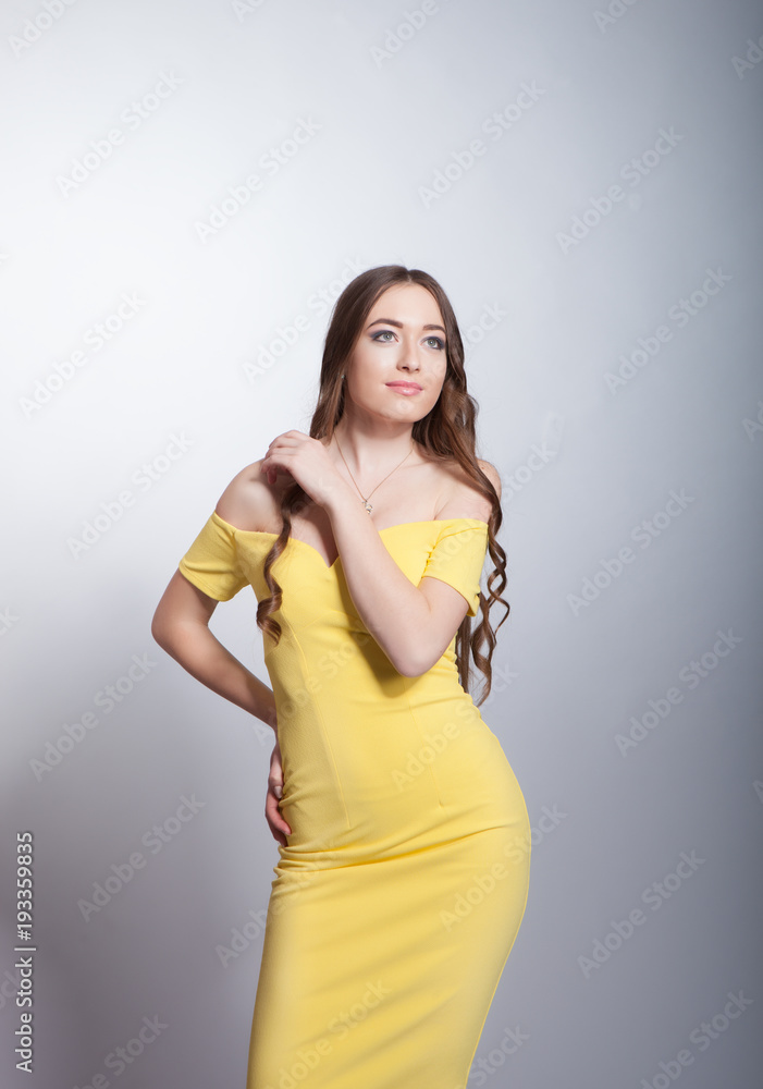 Beautiful girl in a yellow dress on a gray background in the studio Beautiful girl in a yellow dress on a gray background in the studio