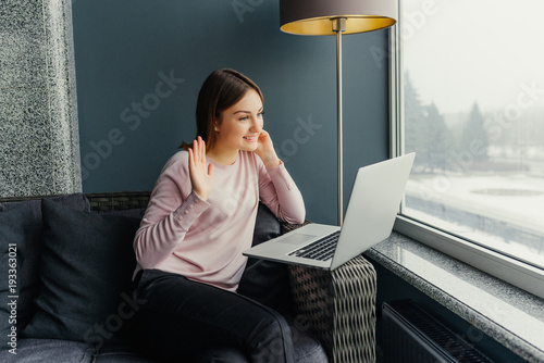 Smiling young woman using laptop and making video call in cafe.