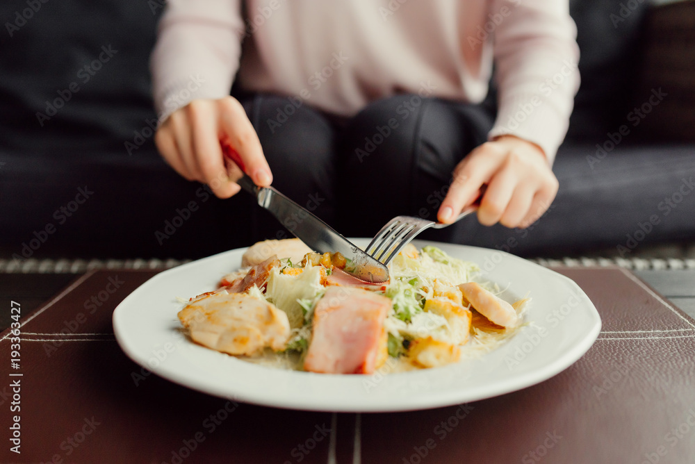 Lunch at restaurant. Female hands using fork and knife for caesar salad. Close-up view.