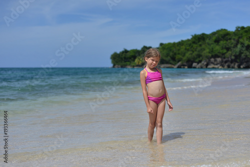 Little blonde Caucasian girl is on the beach with gold sand and blue water somewhere in Caribbean.  