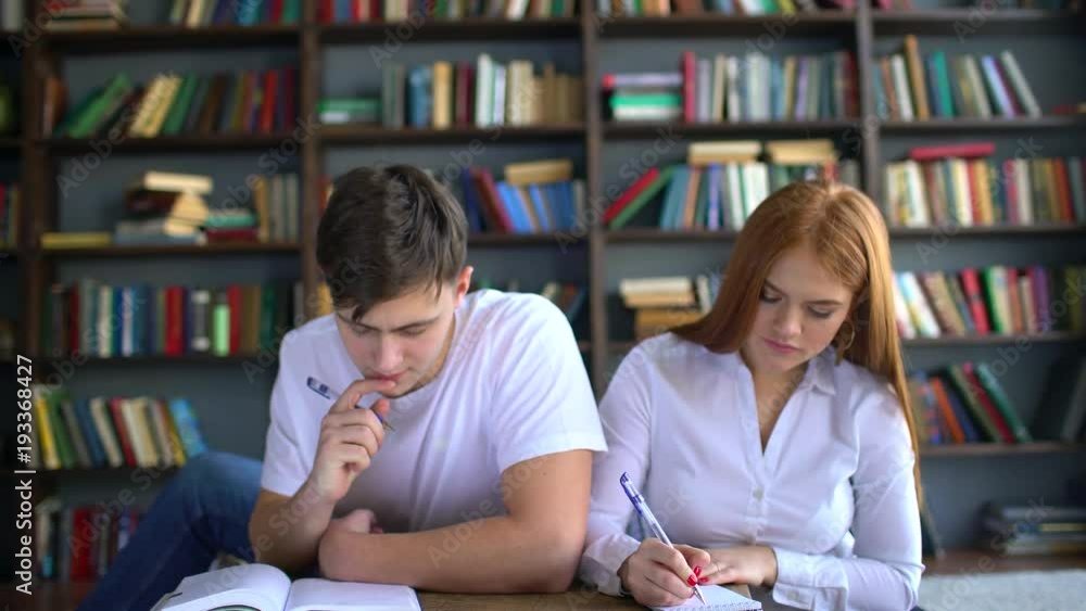 Young couple of students preparing to the exam. 4 k people, knowledge, education and school concept - students with books preparing to exam in library. Young couple of students preparing to the exam. 4 k people, knowledge, education and school concept - students with books preparing to exam in library.