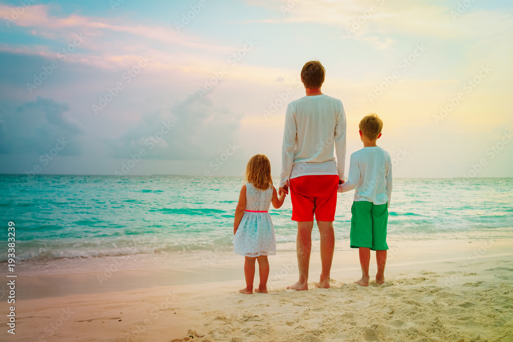 father with son and daughter holding hands at sunset beach