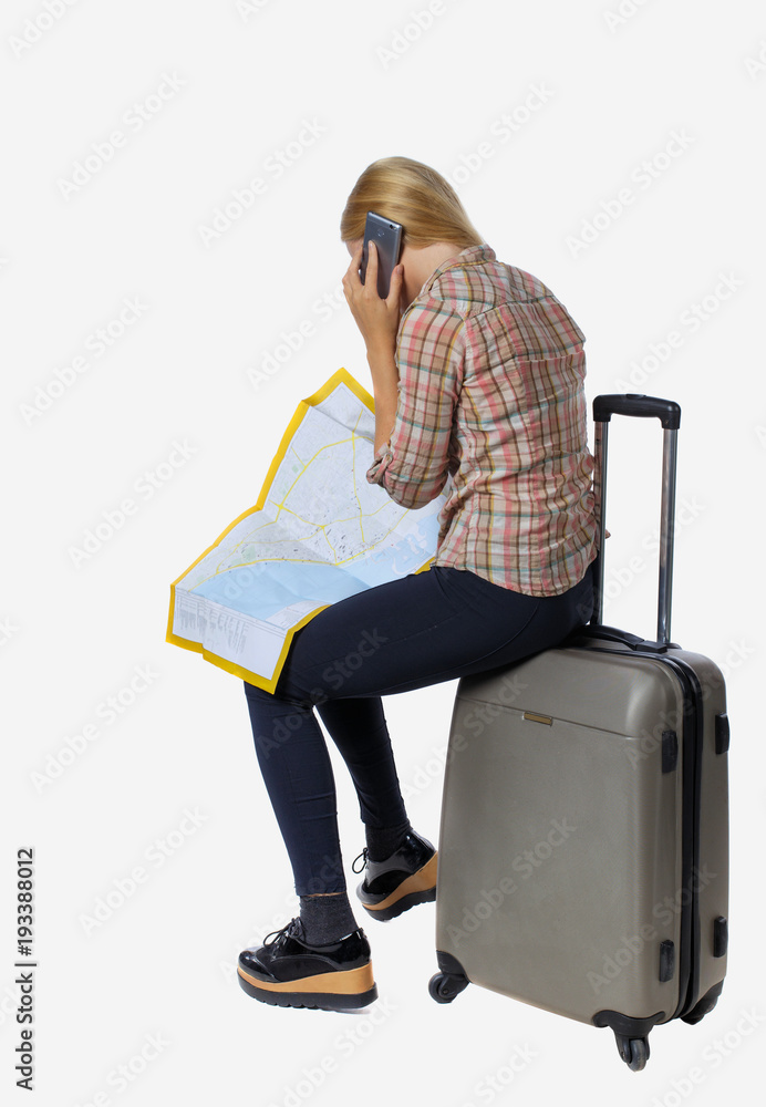 back view of woman traveler sitting on their suitcases and looking for a route map, talking the phone. back view of woman traveler sitting on their suitcases and looking for a route map, talking the phone.