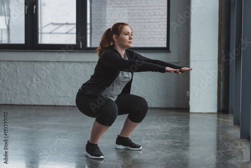 Curvy girl doing squat in gym