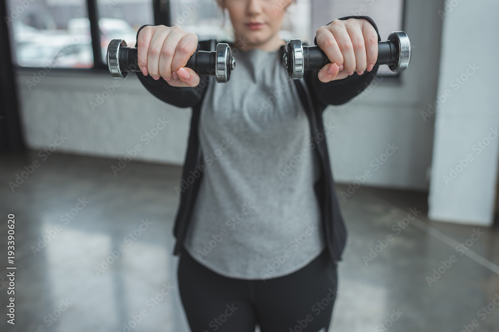 Obese girl exercising with dumbbells in gym
