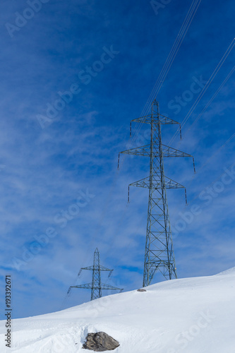 two electricity pylons in winter, snow, stone, sunny blue cloudy sky