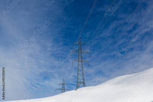 two electricity pylons in winter, snow, sunny blue sky, clouds