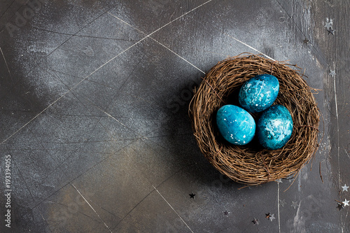 Easter eggs in nest painted by hand in blue color on dark background