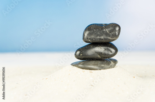 Three black stones in the sand  blue sky background