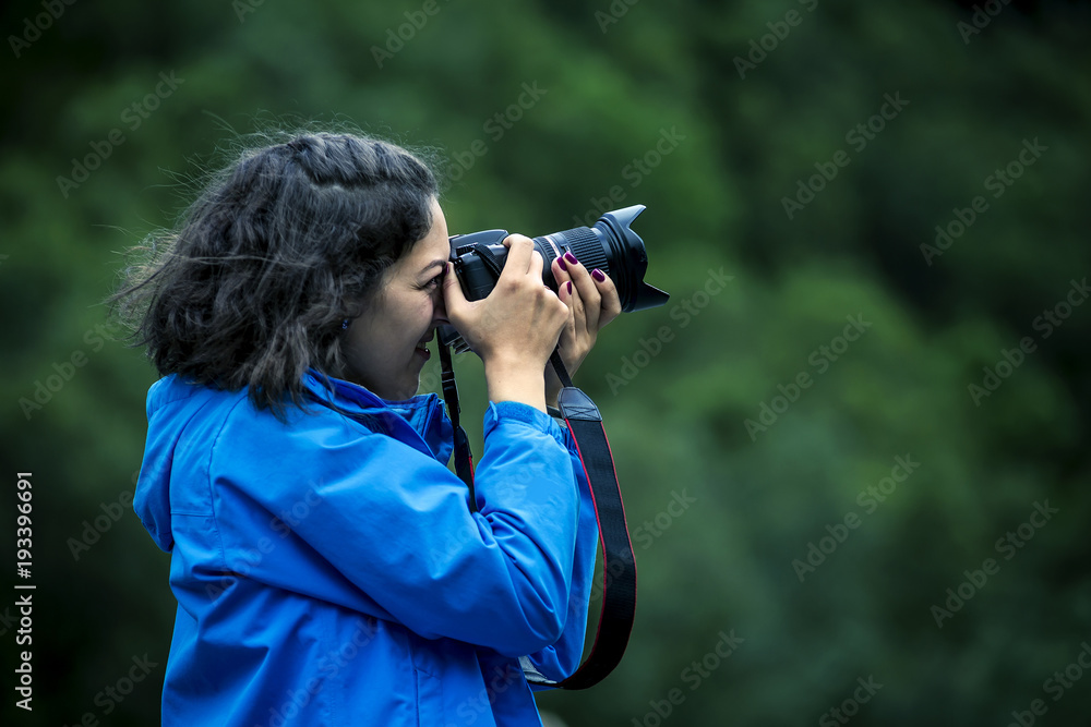 Young woman in blue jacket and curly hair is taking a picture, close up, soft focus, Norway. Young woman in blue jacket and curly hair is taking a picture, close up, soft focus, Norway.