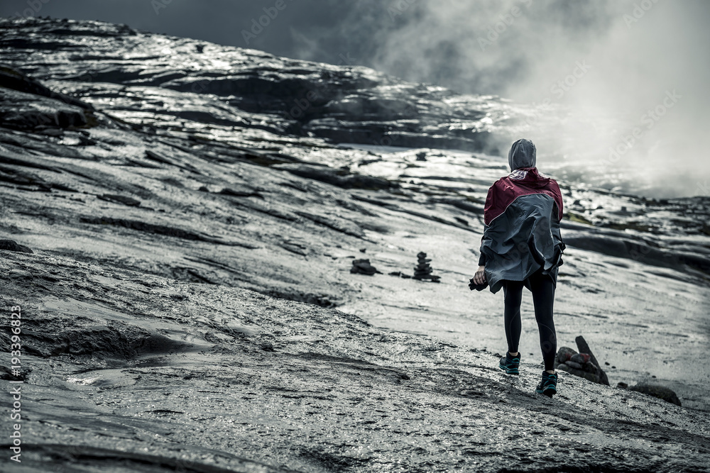 Silhouette of young woman in raincoat walking along the plateau through the foggy place on the way to Kjeragbolten, Norway. Silhouette of young woman in raincoat walking along the plateau through the foggy place on the way to Kjeragbolten, Norway.