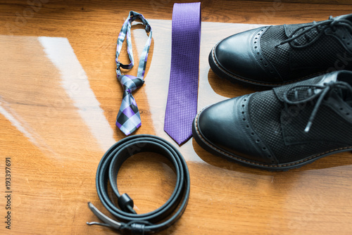 The groom's and a dog’s wedding accessories. Lilac neck tie and a black leather belt and black shoes on a wooden background.