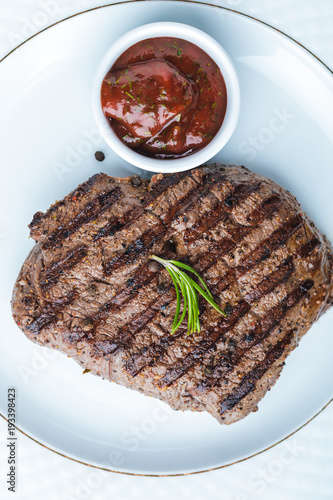 top view of tasty grilled steak with rosemary and bbq sauce on plate