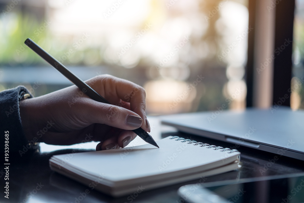 Closeup image of a woman's hands writing on notebook on the table Closeup image of a woman's hands writing on notebook on the table