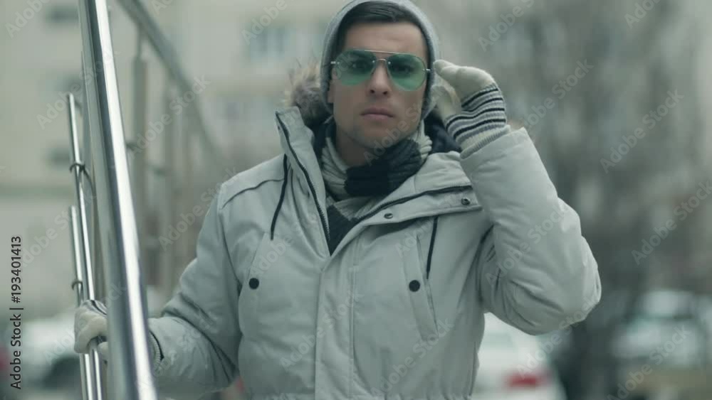 A guy in a bright jacket is standing, looking, adjusting glasses A guy in a bright jacket is standing, looking, adjusting glasses