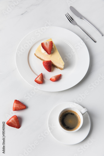 Coffee cup with cheesecake and sliced strawberries on plate