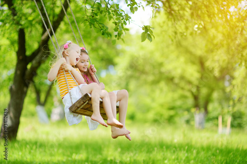 Foto Two cute little sisters having fun on a swing together in beautiful summer garde