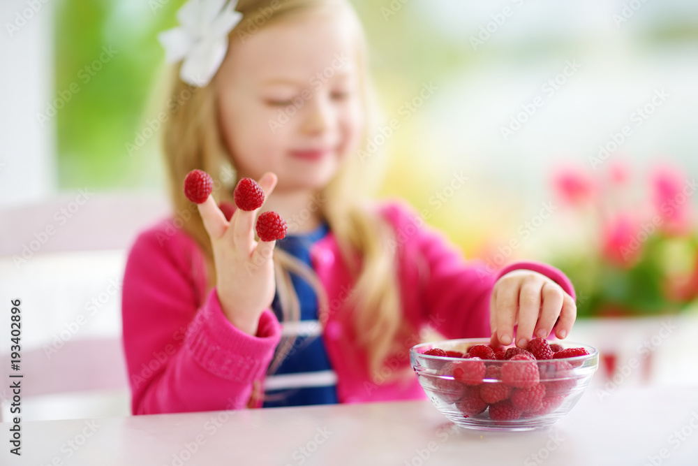 Pretty little girl eating raspberries at home. Cute child enjoying her healthy organic fruits and berries. Pretty little girl eating raspberries at home. Cute child enjoying her healthy organic fruits and berries.