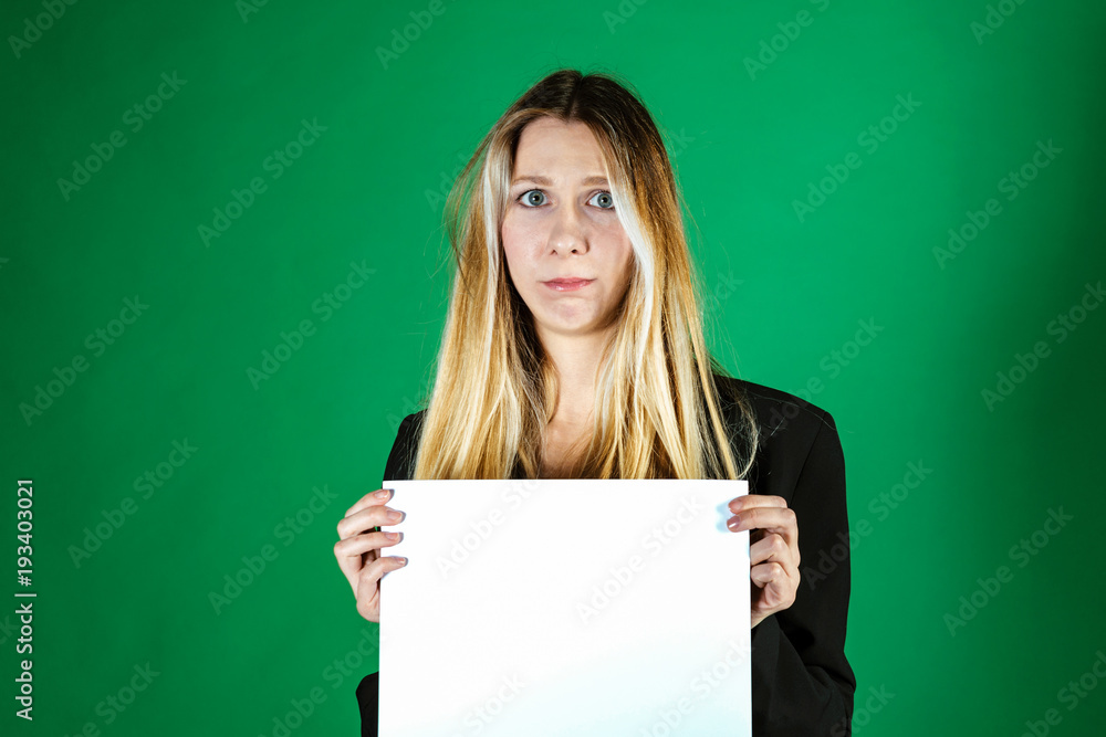 Attractive blonde business woman holding white banner with copy space for additional text or graphic. Frustrated model. Girl is posing on a green background Attractive blonde business woman holding white banner with copy space for additional text or graphic. Frustrated model. Girl is posing on a green background
