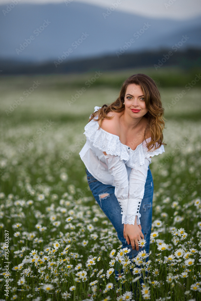 Fototapeta premium Beautiful happy smiling woman on the camomile field is wearing white dress, spring time
