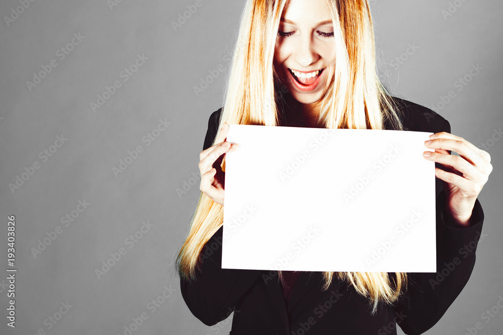 Naklejka premium Attractive blonde business woman holding white banner with copy space for additional text or graphic. Girl is posing on a grey background. Trendy style