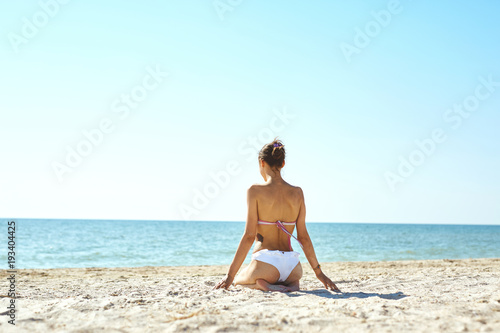 beautiful sexual young woman in white bikini stands on the beach against the sea and sky at sunny day. happy woman enjoys summer vacation and goes to swim in the sea. Back view