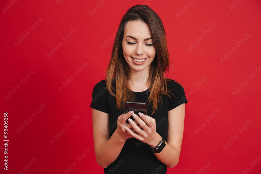 Contented woman with smile typing text message or social networking on smartphone, over red background Contented woman with smile typing text message or social networking on smartphone, over red background